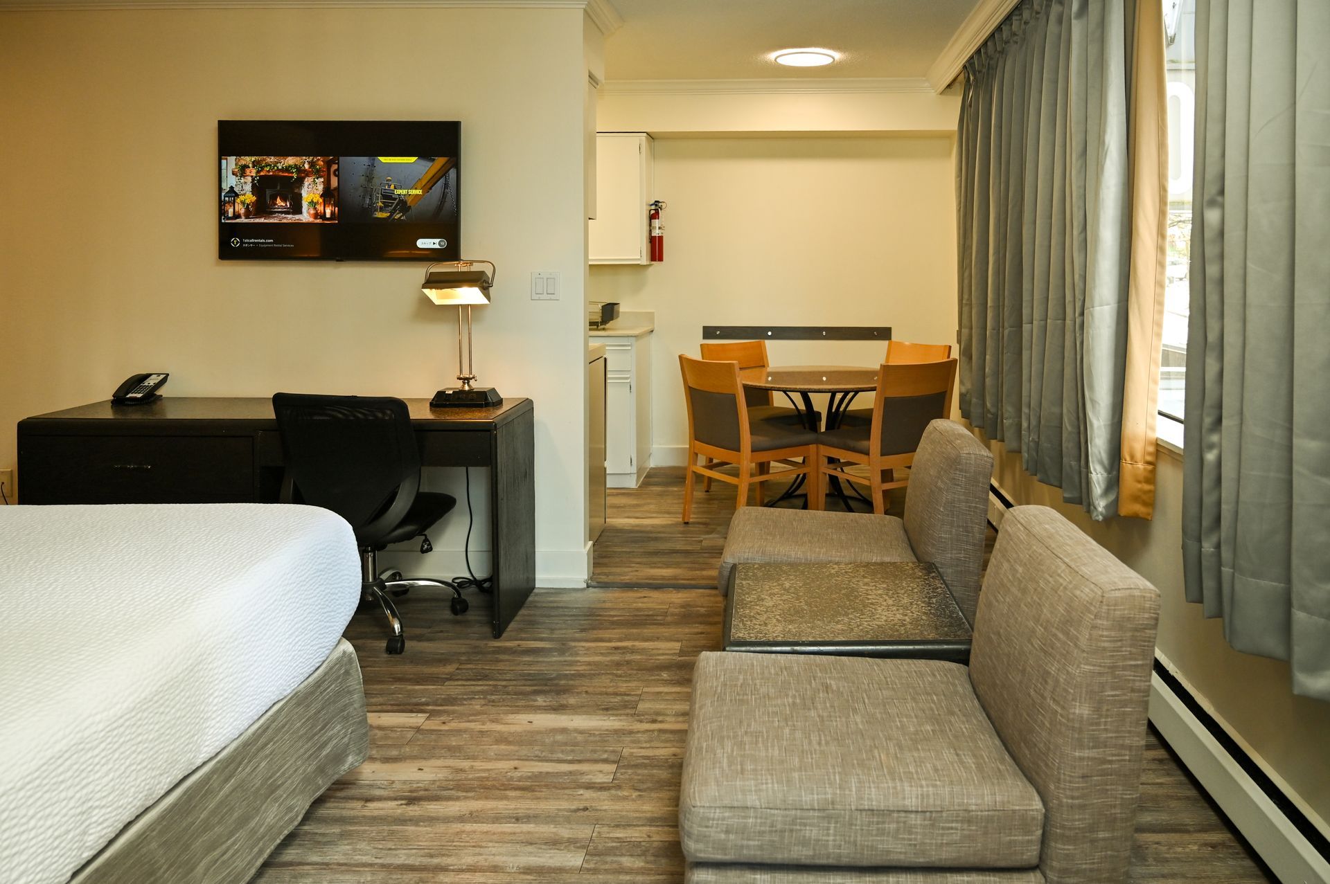 A hotel room featuring a bed, a desk with a chair, and a small table with chairs near a curtained window.
