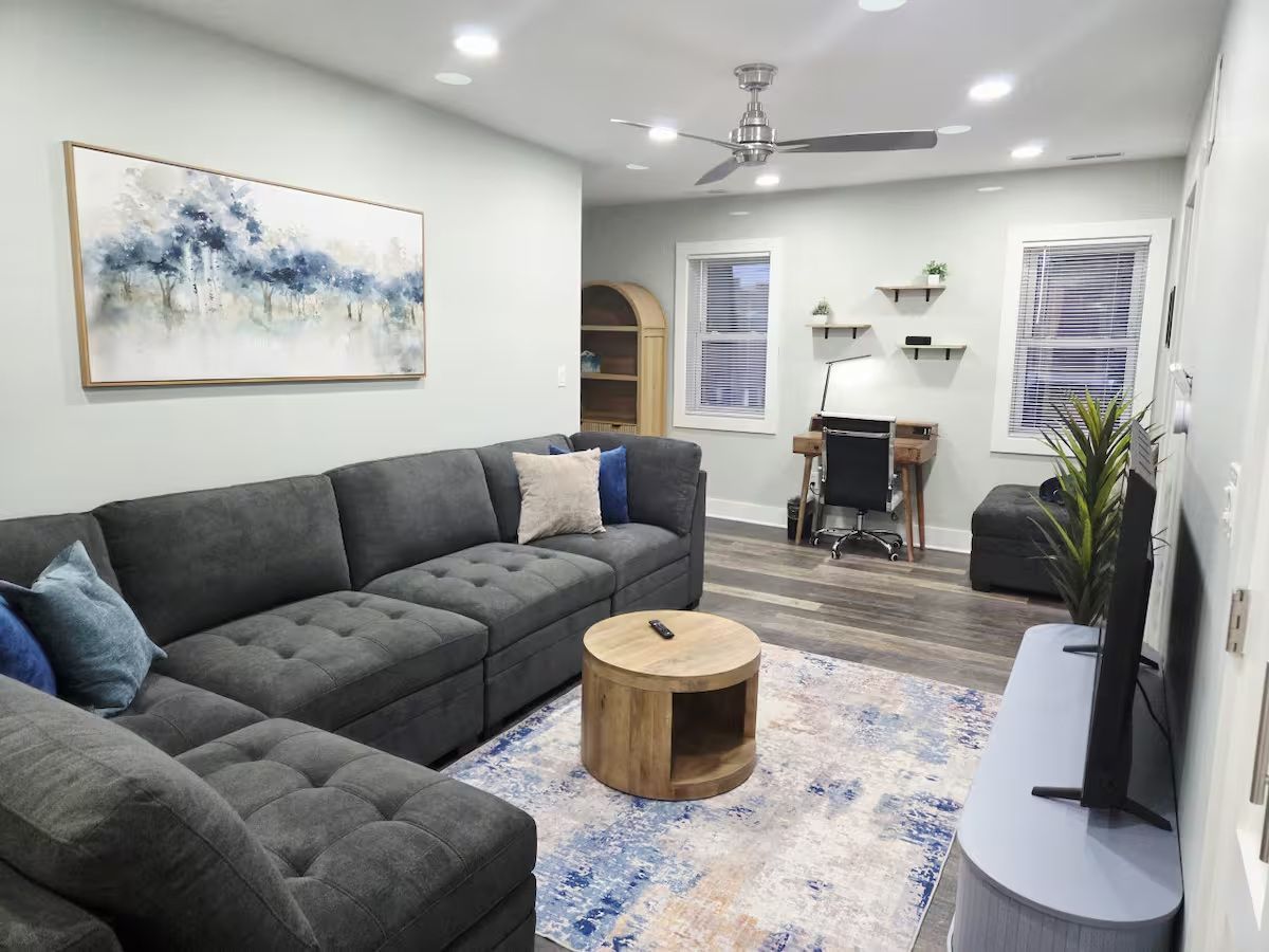 Cozy living room with gray sectional sofa, wooden table, and abstract art; desk area.