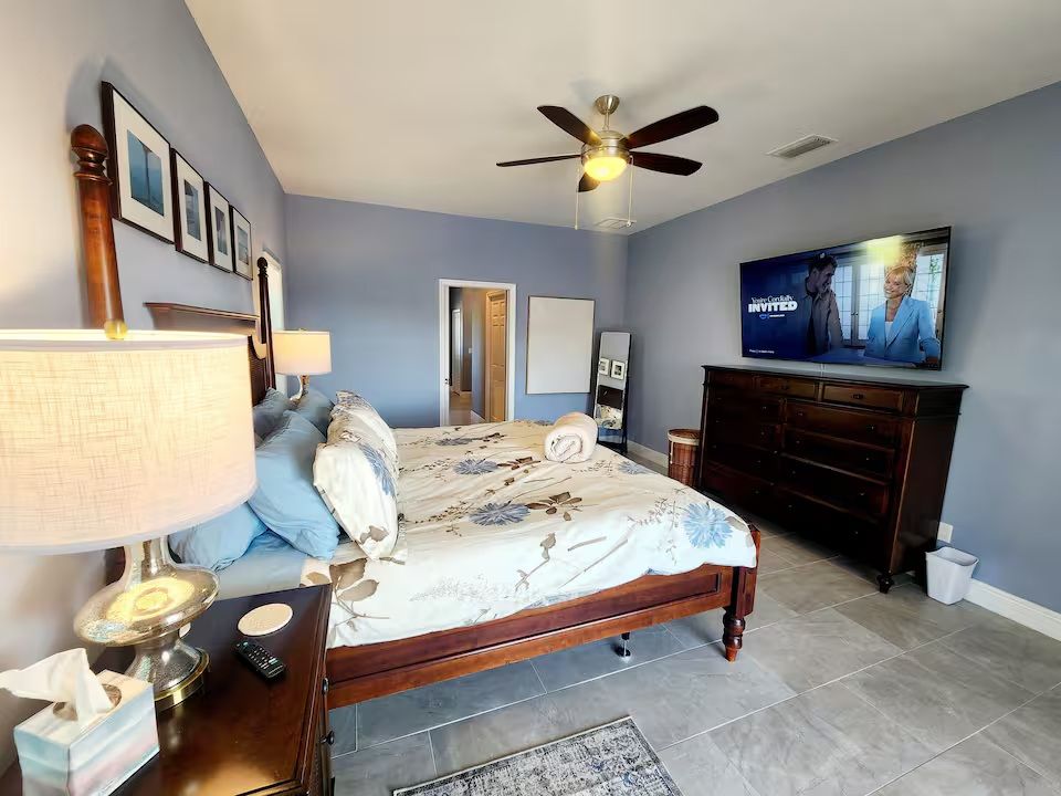 A bedroom with light blue walls, a wooden bed featuring floral bedding, a dark wood dresser, and a ceiling fan.