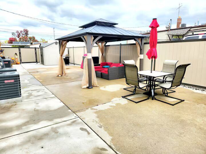 A patio with a gazebo , table and chairs and an umbrella.