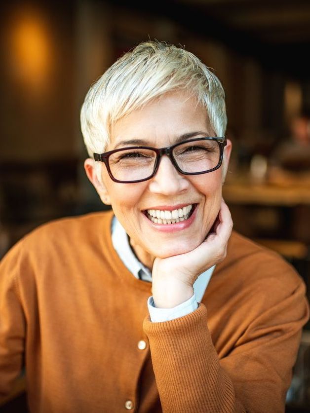 A woman wearing glasses is smiling with her hand on her chin.
