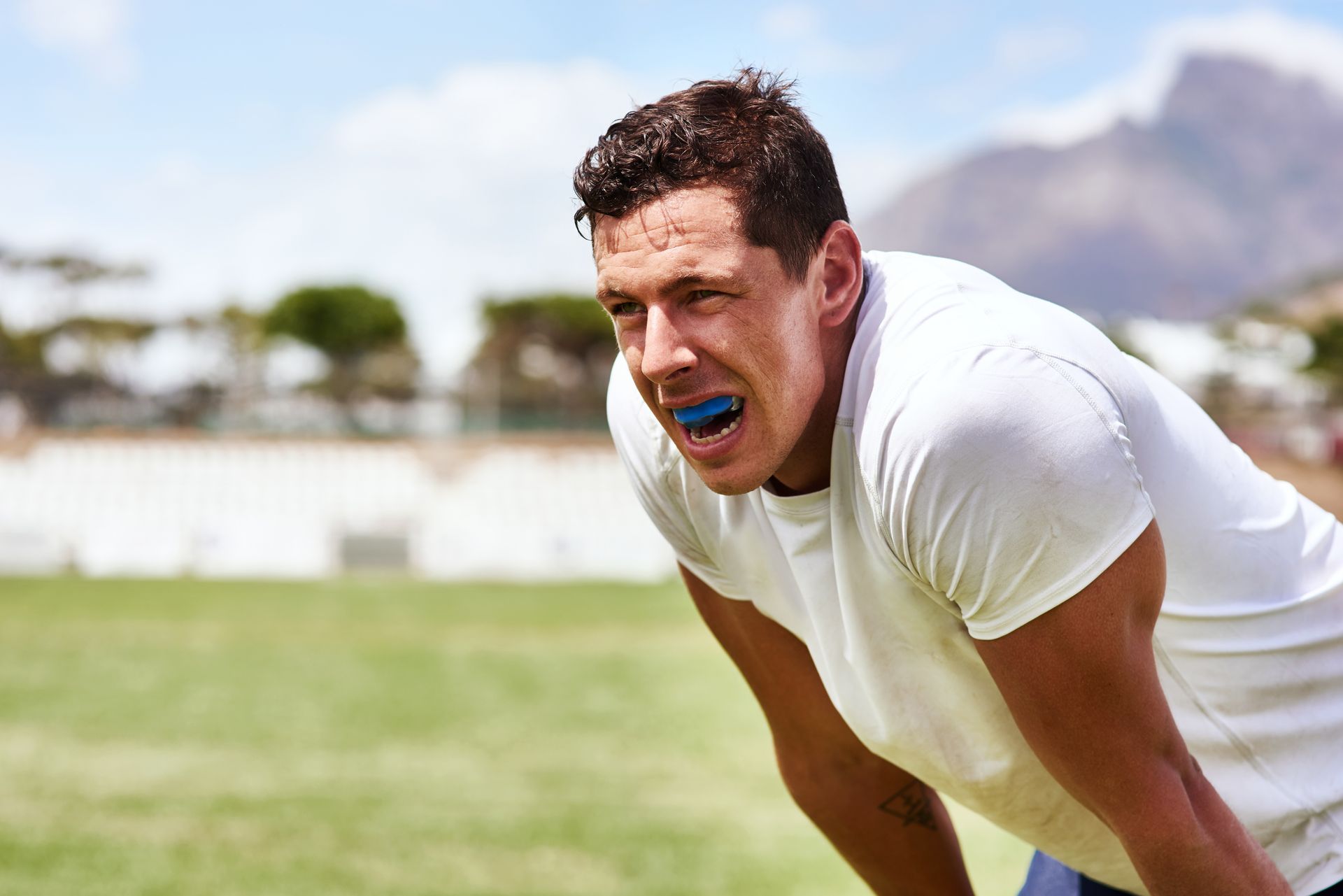 A man wearing a mouth guard is taking a break on a soccer field.