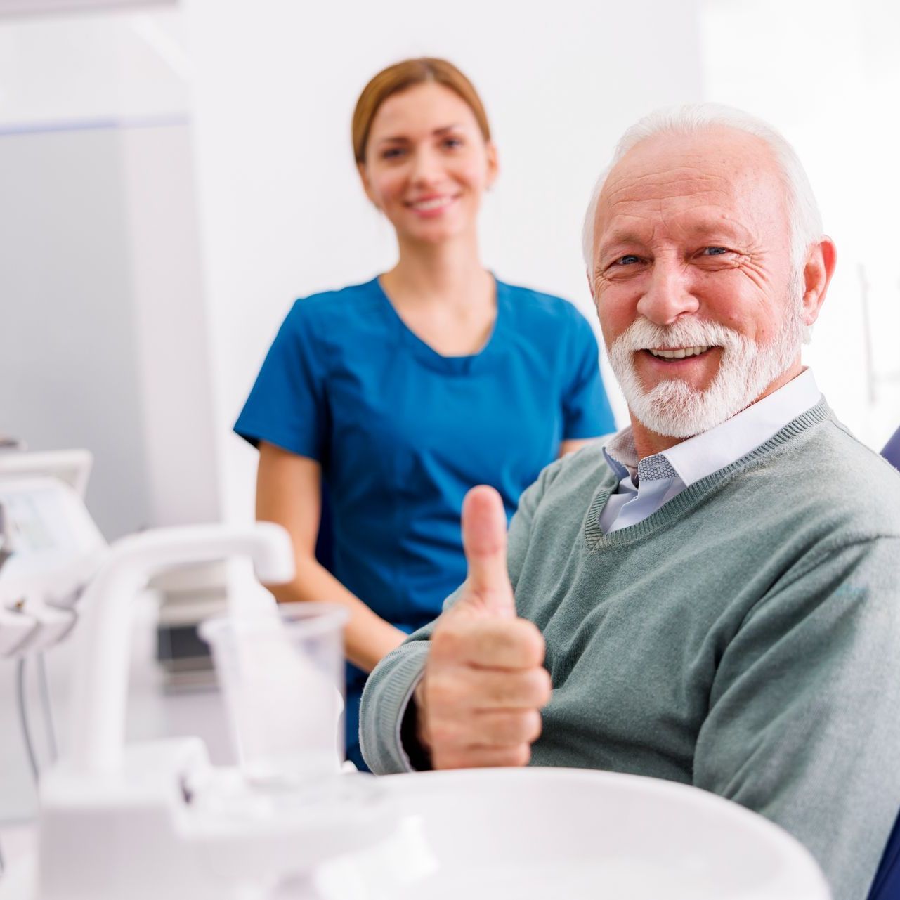 An elderly man is giving a thumbs up in a dental chair.