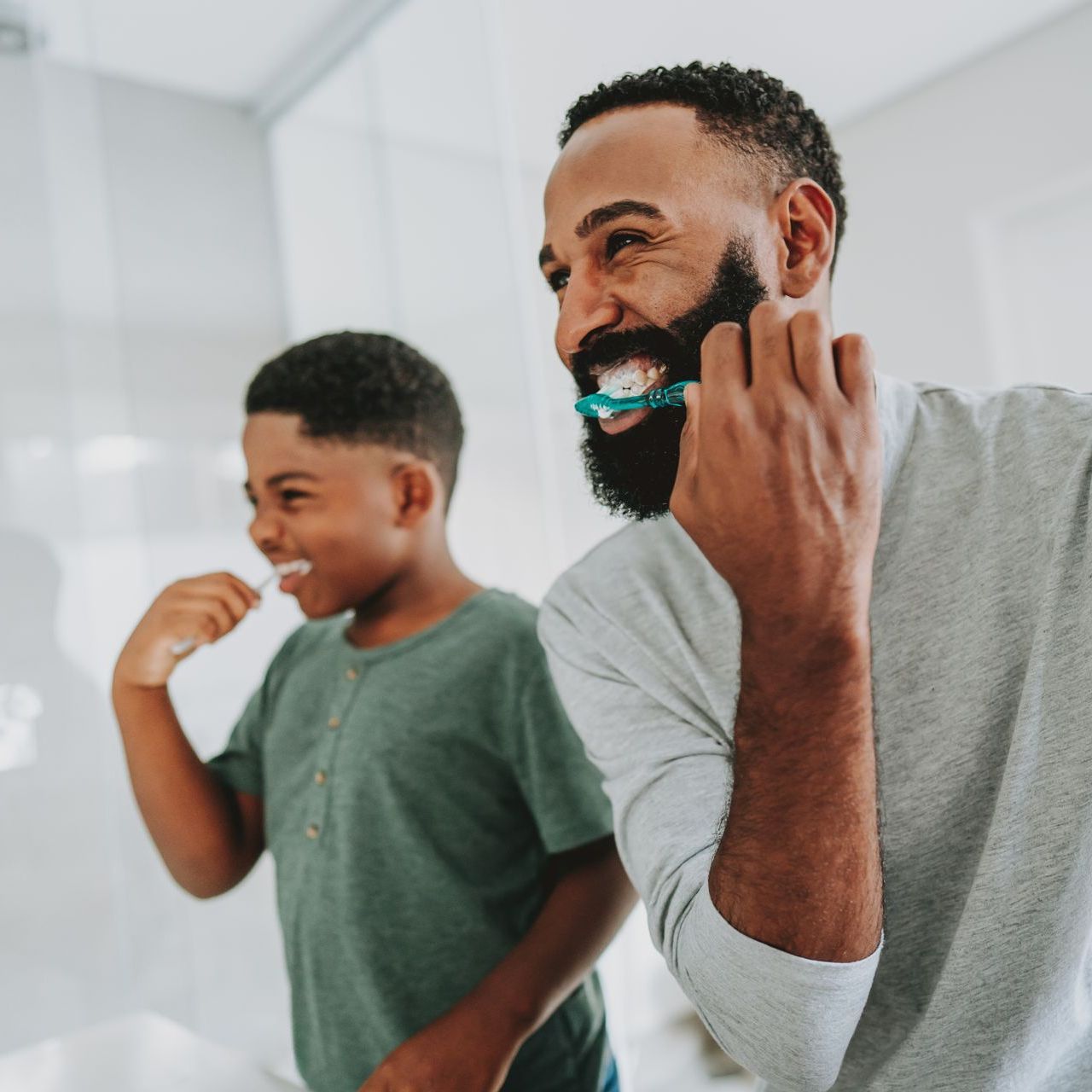 A man with a beard is brushing his teeth next to a young boy