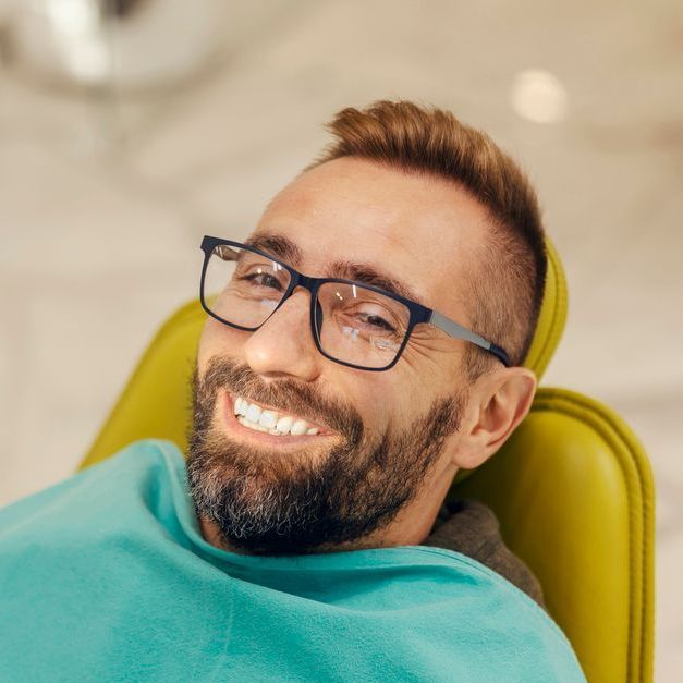 A man wearing glasses is smiling while sitting in a dental chair.