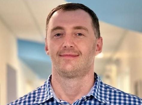 A man in a blue and white checkered shirt is smiling for the camera.