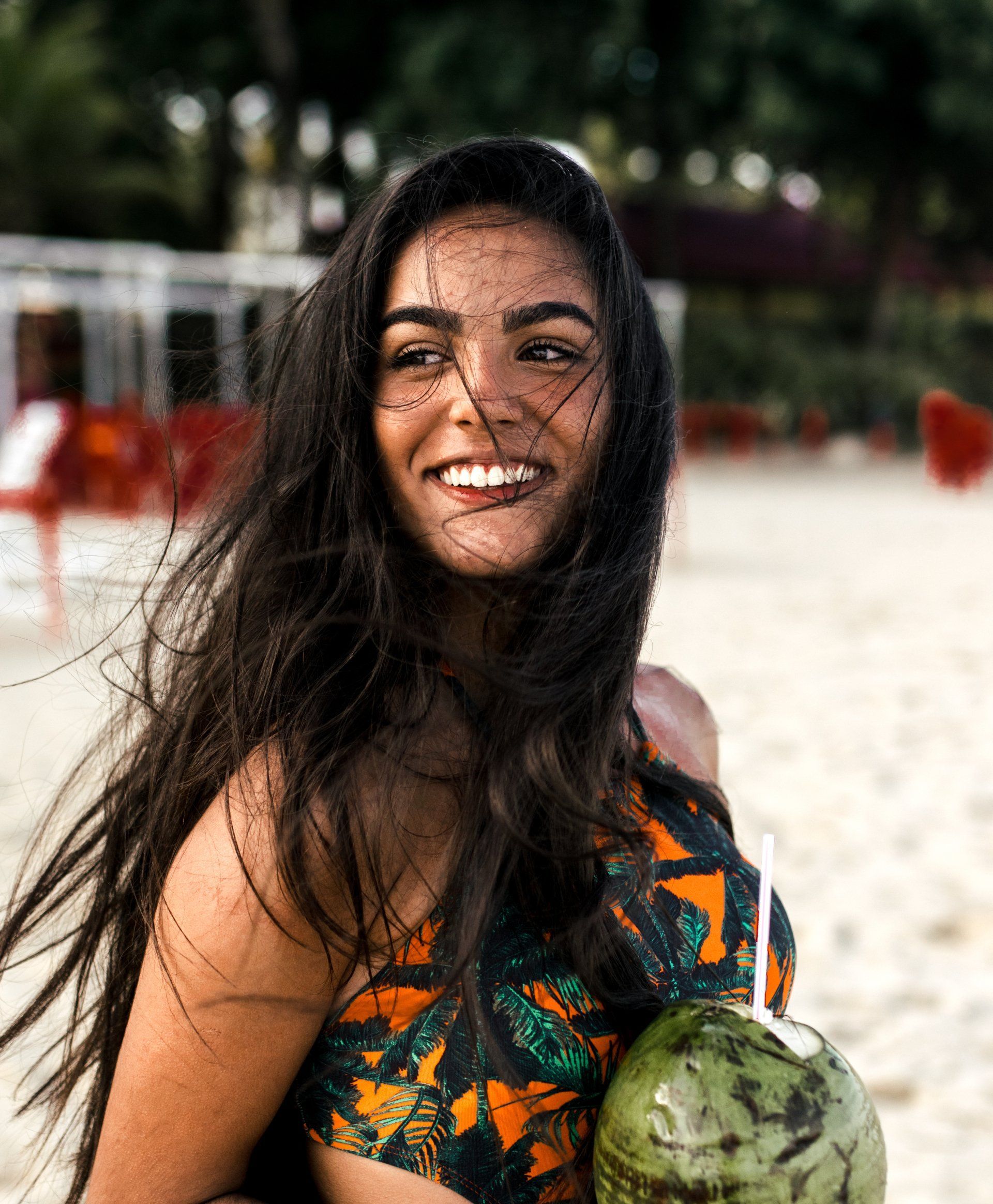 A woman in a bikini is holding a coconut on the beach and smiling.