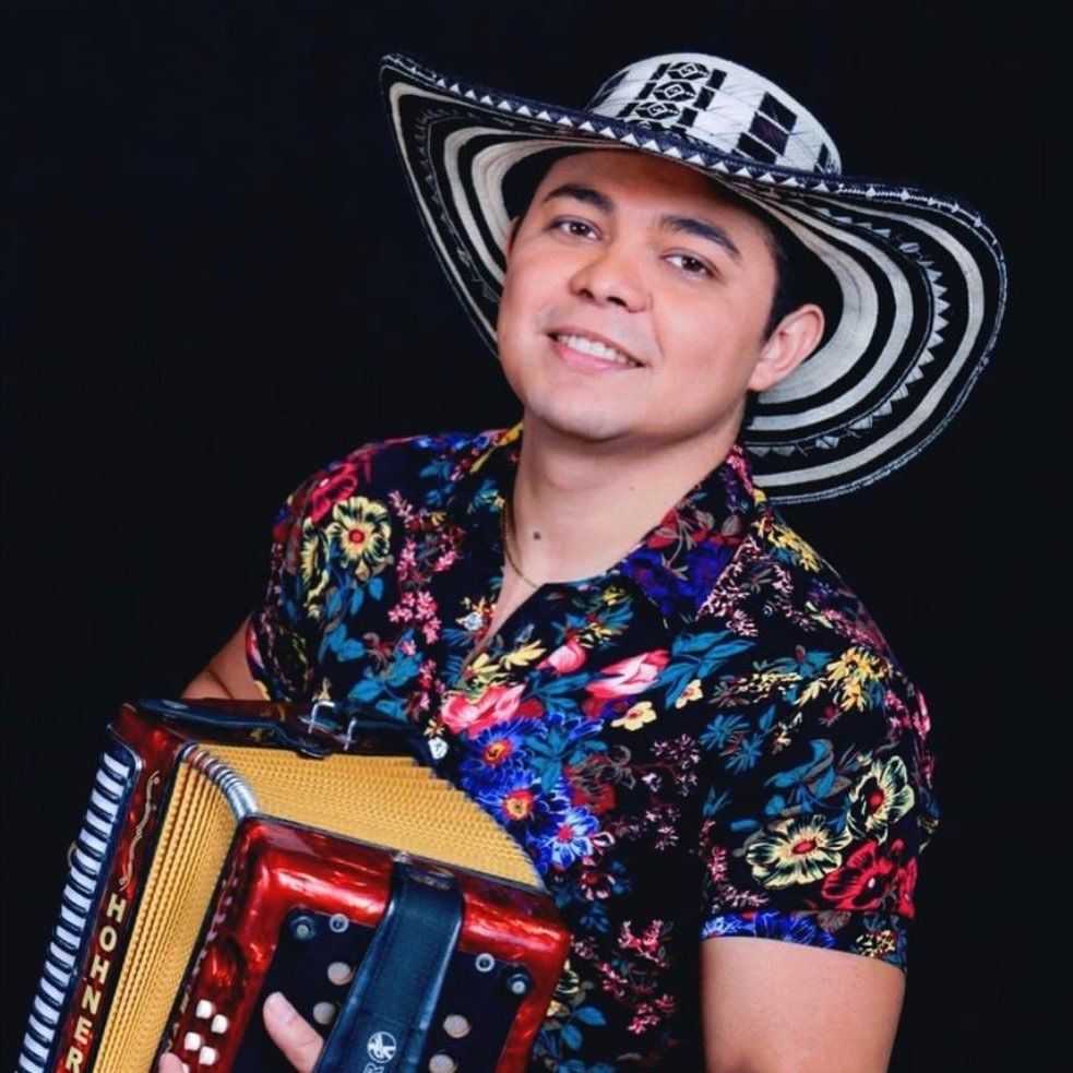 Un hombre con una camisa colorida toca el acordeón en el escenario, usando un sombrero.