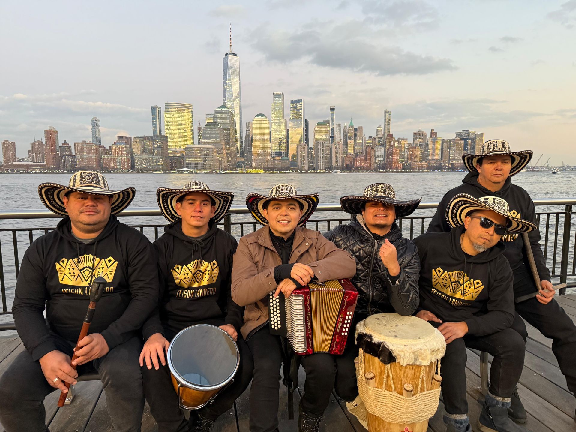 Un grupo de seis músicos con sombreros posan frente al horizonte de la ciudad de Nueva York