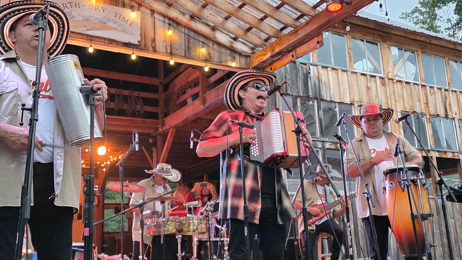 Una banda musical colombiana se presenta al aire libre en un escenario, tocando instrumentos.