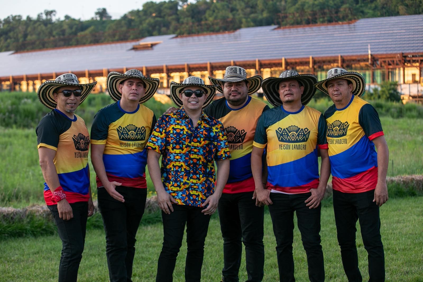 Seis hombres con sombreros de paja y camisetas coloridas con la bandera colombiana posan al aire libre.