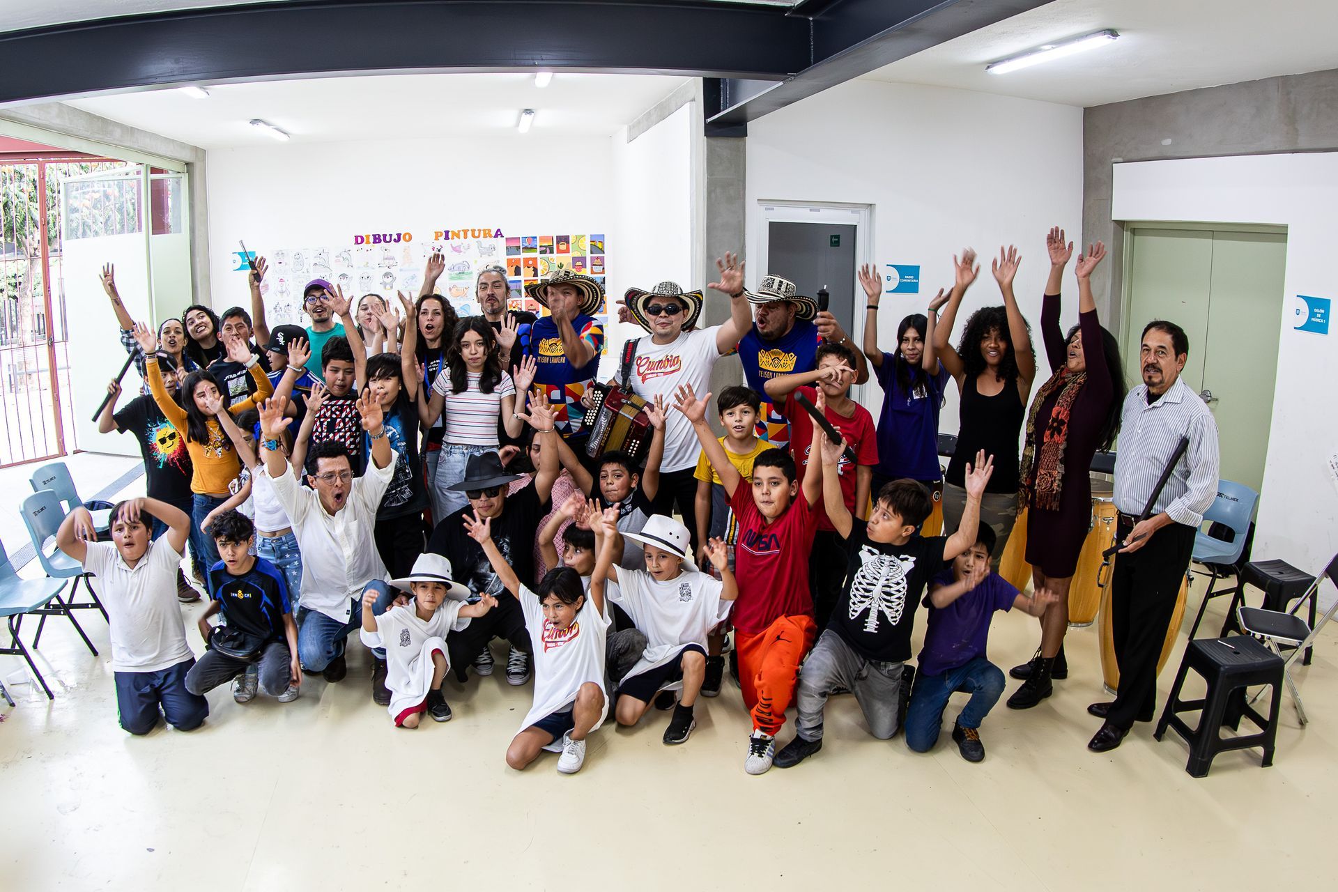 Grupo de personas, en su mayoría niños, animando con los brazos en alto en una sala muy iluminada.