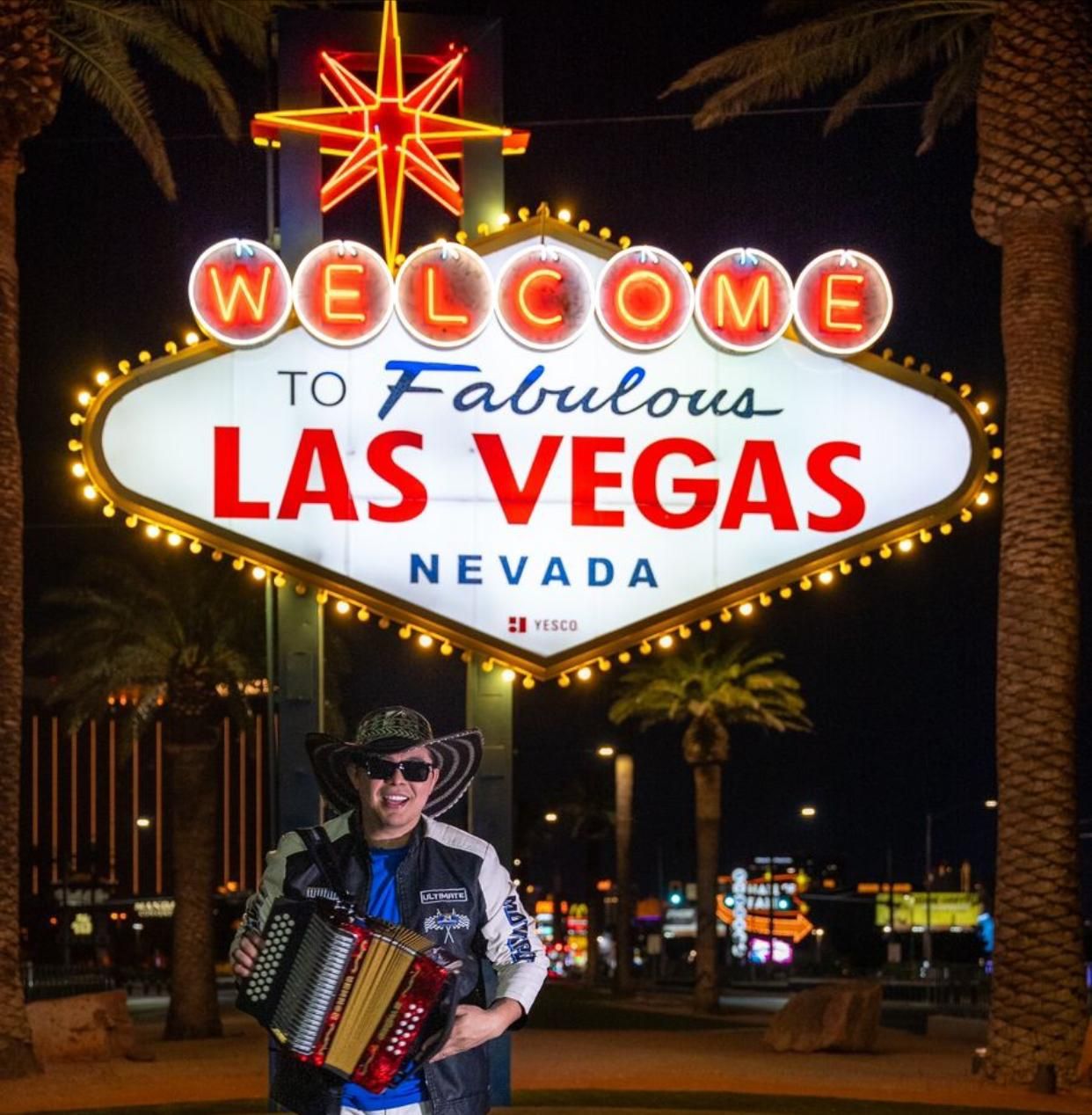 Persona con un acordeón posa frente al cartel de Las Vegas por la noche.
