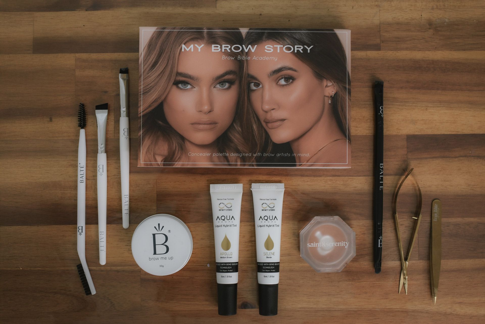 Brow makeup kit on a wooden surface, featuring brushes, tools, and a palette with two women's faces.