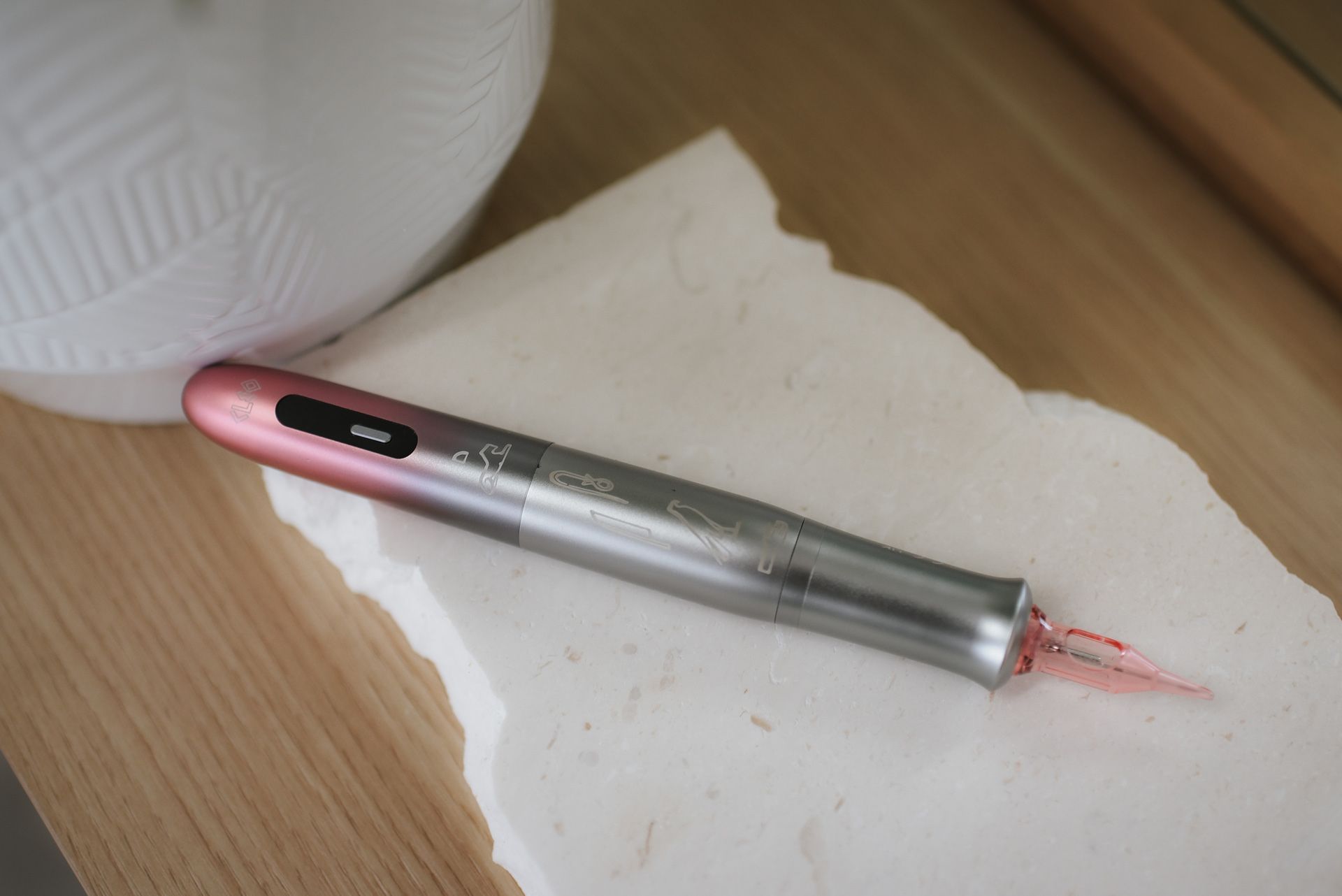 A silver and pink micro-needling pen on a white stone, on a light wood surface.