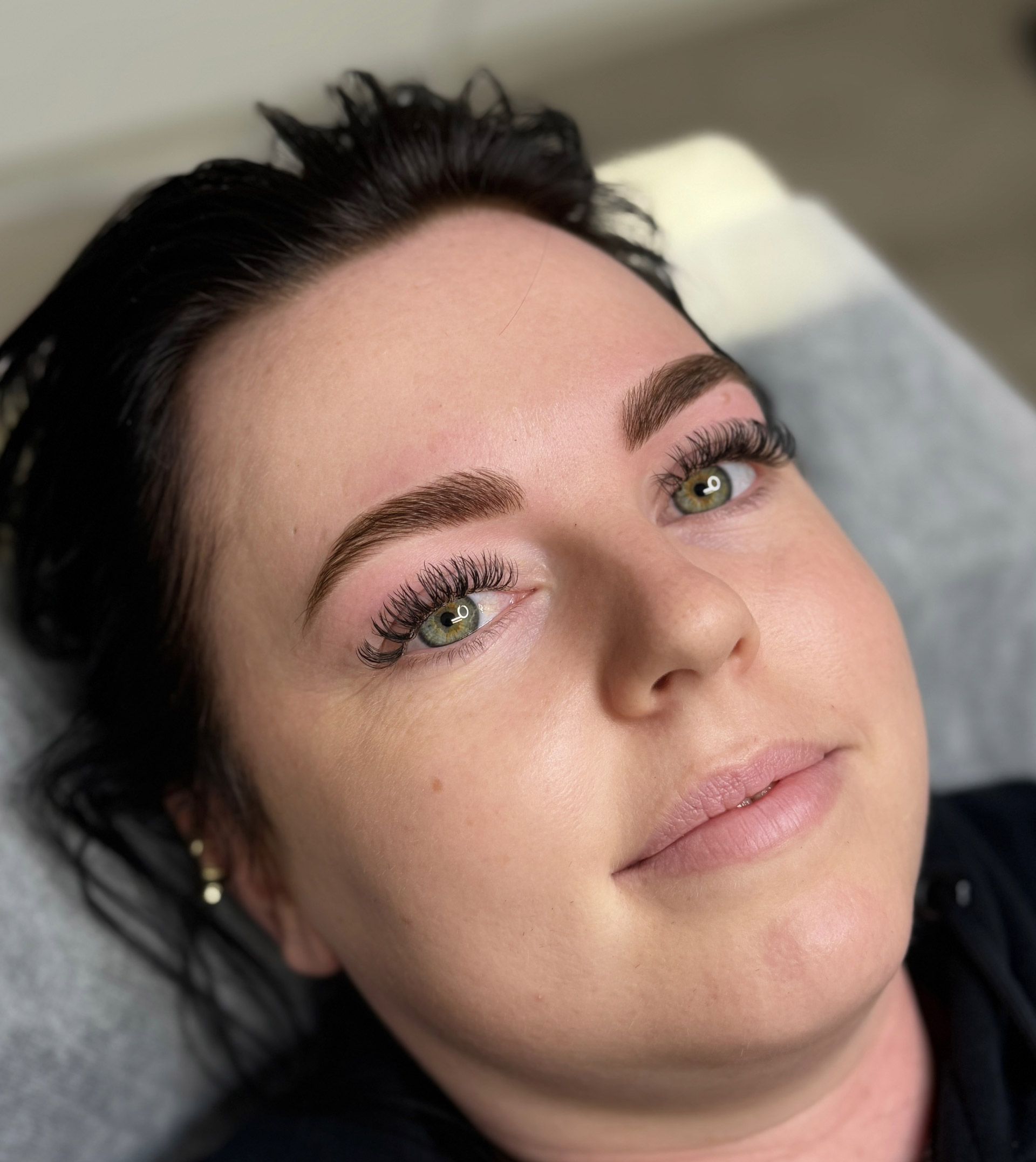 Woman with dark hair and eyebrows, lying down. She has semi-permanent makeup.