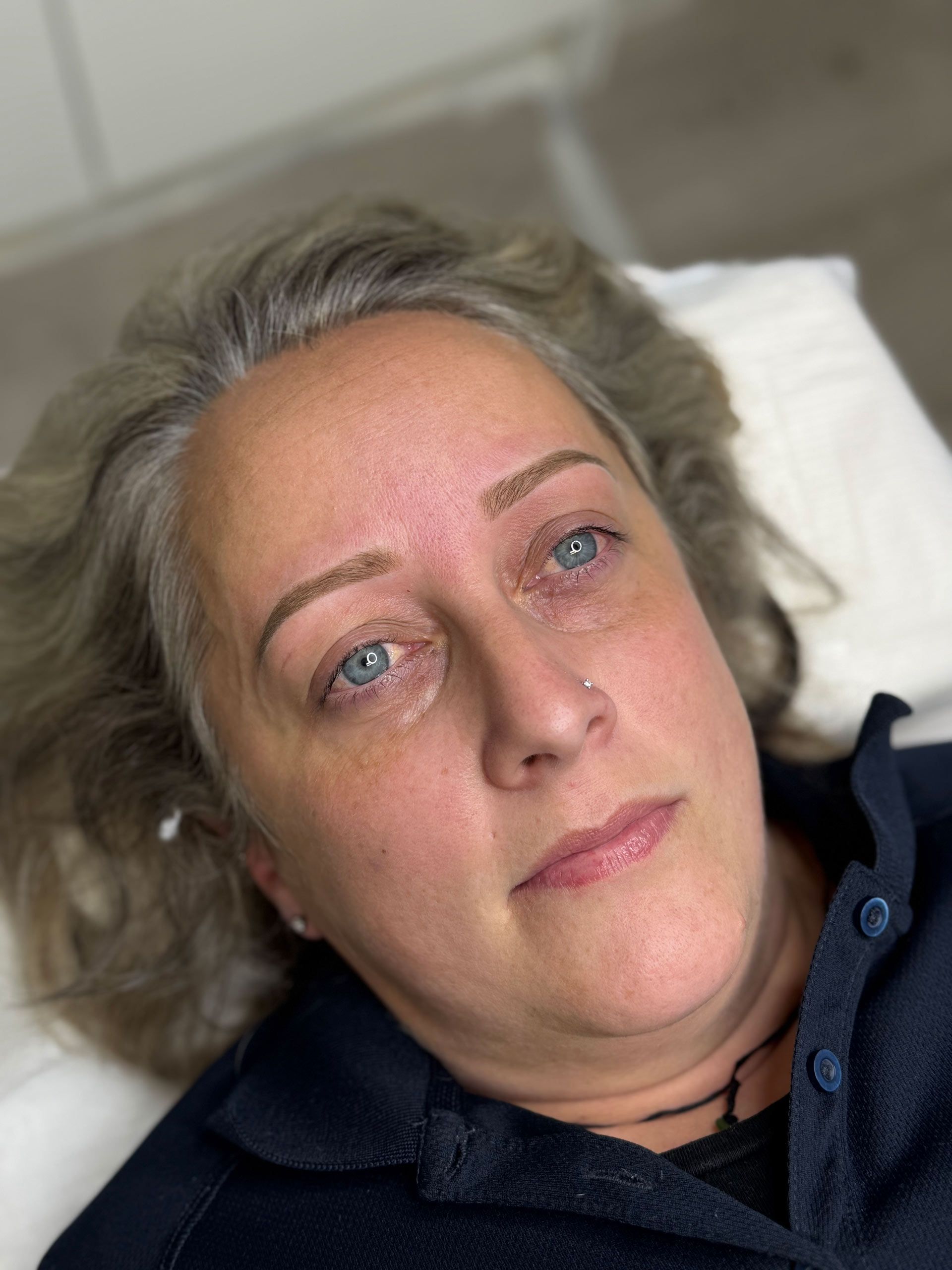 Woman with light brown eyebrows, blue eyes, lying down, looking at the camera.