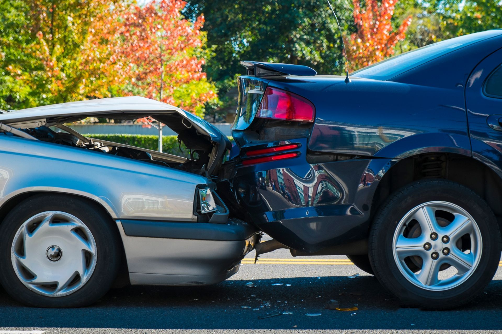 Two cars involved in a rear-end collision on a road; the silver car's front is damaged, while the blue car's rear is dented.