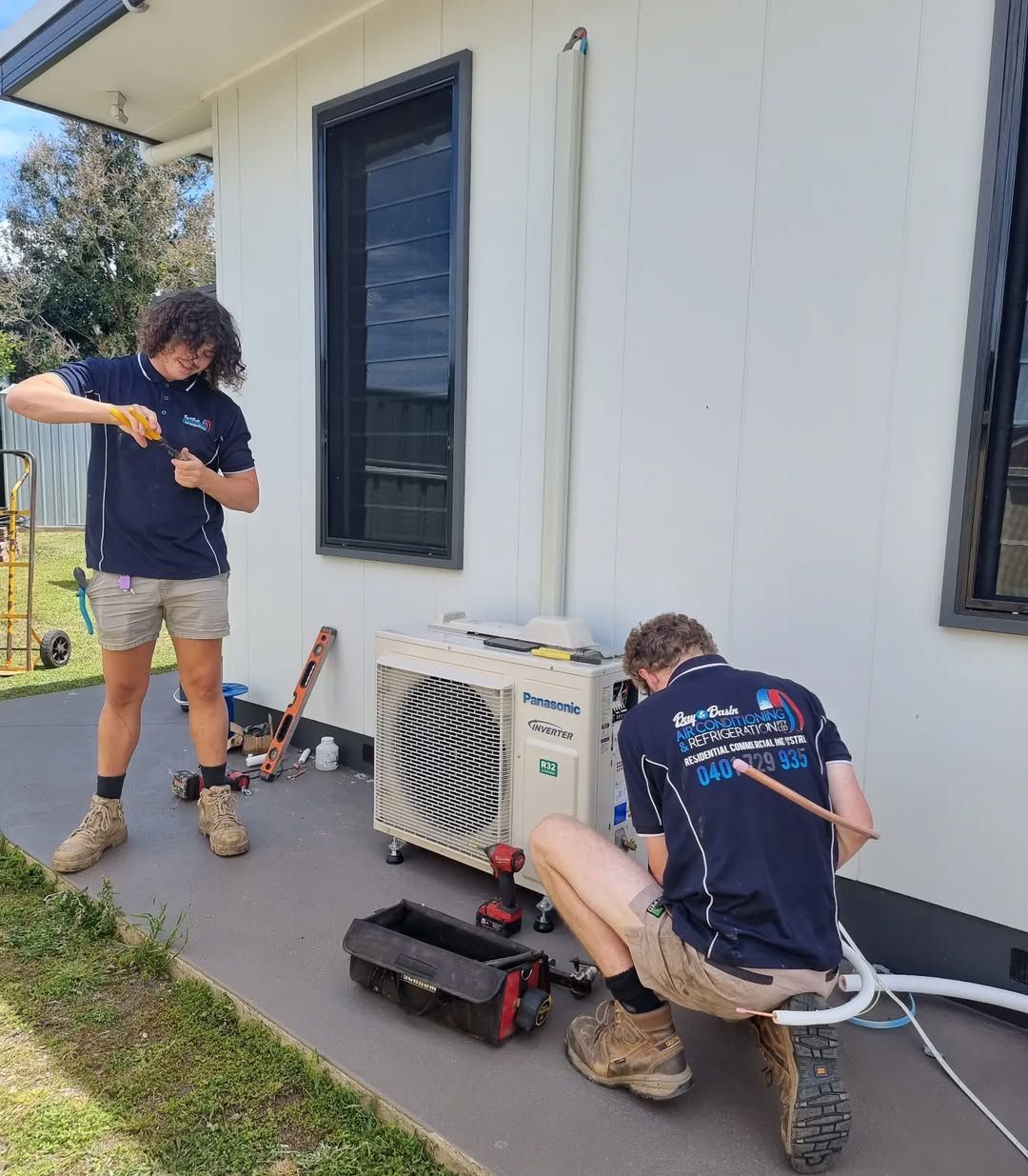 Two Technicians Installing an Outdoor Heat Pump Unit — Bay & Basin Air Conditioning & Refrigeration Pty Ltd in St Georges Basin, NSW