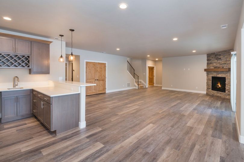 Open-concept living space with kitchen, fireplace, stairs. Gray cabinets, wood floors, neutral walls.