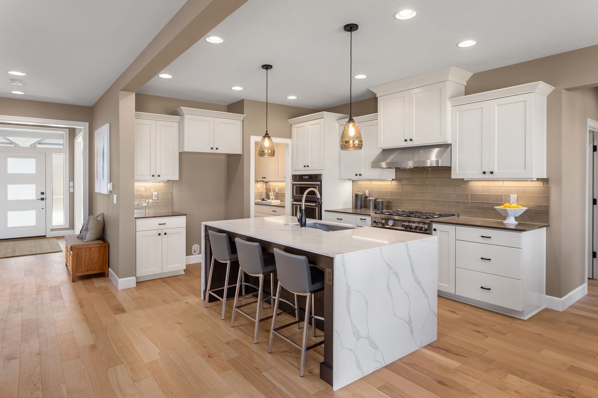 Modern kitchen with white cabinets, marble island, and wood flooring.