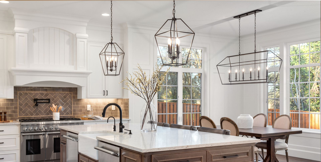 Elegant kitchen with white cabinets, marble countertops, and black metal light fixtures.