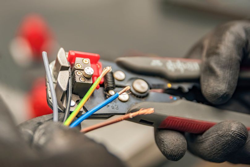 Hands in gloves using wire strippers to prepare electrical wires.