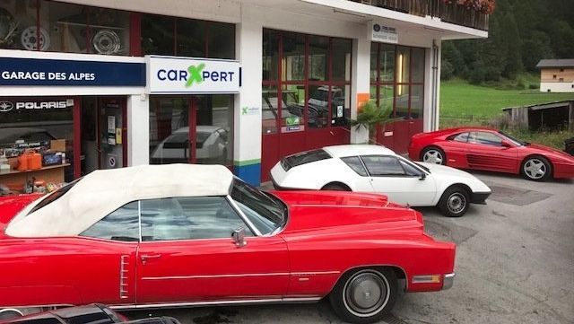 Une cadillac rouge est garée devant un garage.
