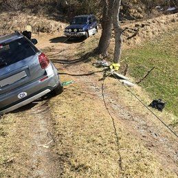 Une voiture est assise sur le bord d'un chemin de terre à côté d'un arbre.