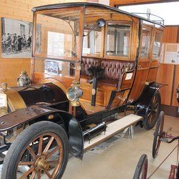 Une vieille voiture se trouve dans un musée à côté d'une calèche.