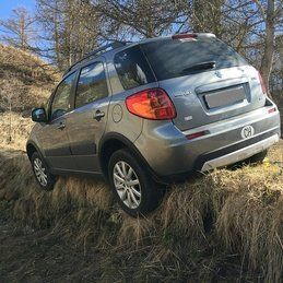 Une suzuki sx4 est coincée dans l'herbe sur une colline.
