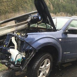 Un SUV bleu avec son capot ouvert est assis sur le bord de la route.