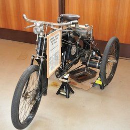 Un vieux vélo à trois roues est posé sur un plancher en bois.