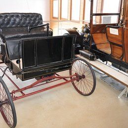 Une vieille voiture avec une voiture attachée est assise dans une pièce.