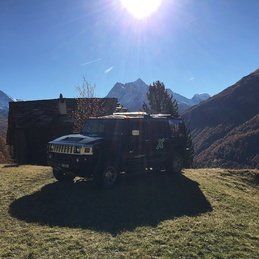 Un hummer h2 est garé au sommet d'une colline herbeuse avec des montagnes en arrière-plan.