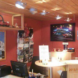 Une pièce avec un bureau, des chaises, un ordinateur et une télévision au mur.