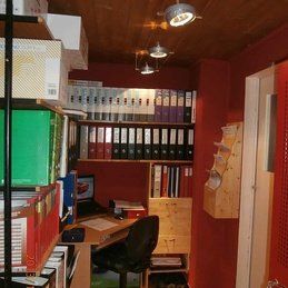 Un petit bureau avec un bureau, une chaise, des étagères et un ordinateur.