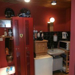 Une salle de bain aux murs rouges, un lavabo, un micro-onde et un miroir.