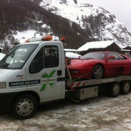 Une voiture rouge est remorquée par une dépanneuse dans la neige.