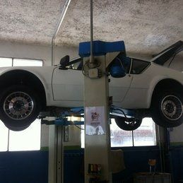 Une voiture blanche est assise au sommet d'un ascenseur dans un garage.