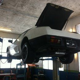 Une voiture blanche est assise sur un ascenseur dans un garage avec le capot relevé.