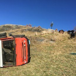 Un camion rouge est renversé sur le côté dans un champ herbeux.