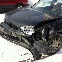 Une voiture noire avec l'avant endommagé est garée dans la neige.