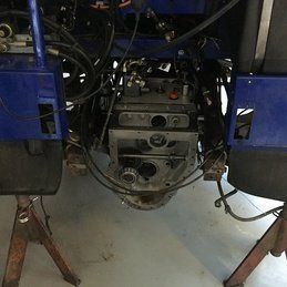 Le moteur d'un tracteur bleu est posé sur un support dans un garage.