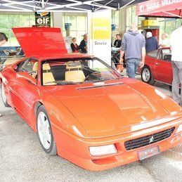 Une voiture de sport rouge avec le capot relevé est garée dans un parking.