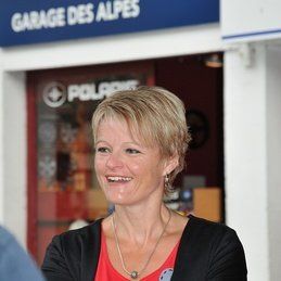 Une femme sourit devant une pancarte du garage des alpes.