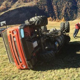 Un tracteur rouge est retourné sur le côté dans un champ herbeux.