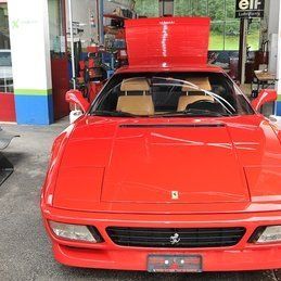 Une Ferrari rouge avec le capot relevé est garée dans un garage.