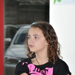 Une jeune fille aux cheveux bouclés porte une chemise rose et noire.