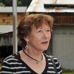 Une femme portant une chemise rayée et des boucles d'oreilles se tient devant un immeuble.